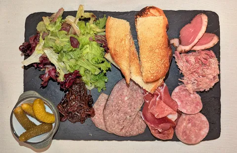Une planche de charcuterie servie sur ardoise, avec du pain grillé