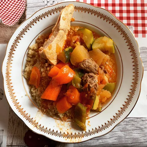 Une assiette de couscous à l'agneau et aux légumes, posée sur une nappe vichy
