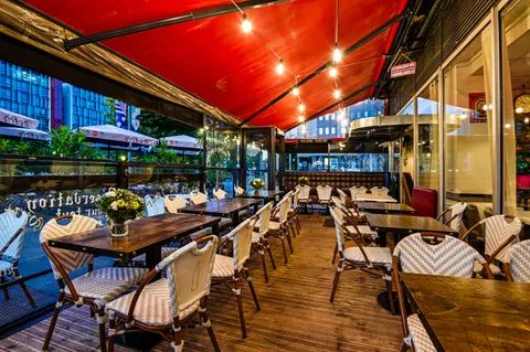 La véranda de la Brasserie L'Escale sous son store rouge, tables en bois et guirlandes d'ampoules